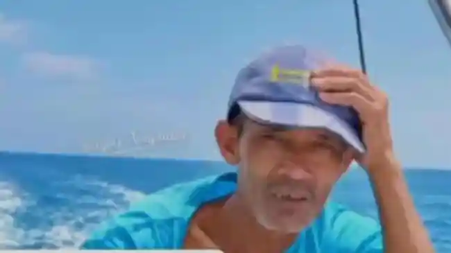 Potret almarhum Surakman kru KM Arupadhatu I mengenakan kaos biru dan topi saat berada di atas kapal cepat di tengah laut.